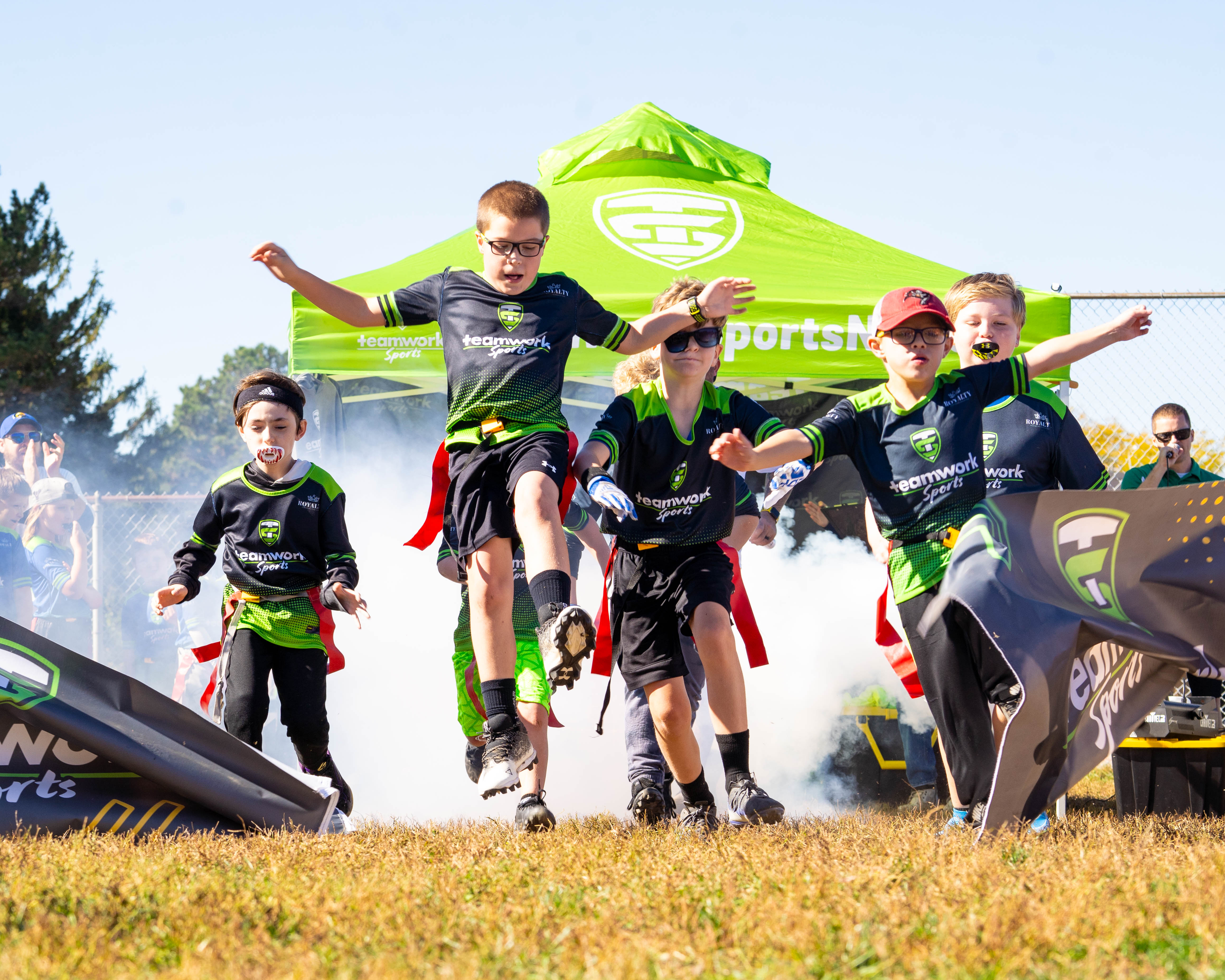 A flag football team bursting through the Teamwork Sports banner on game day