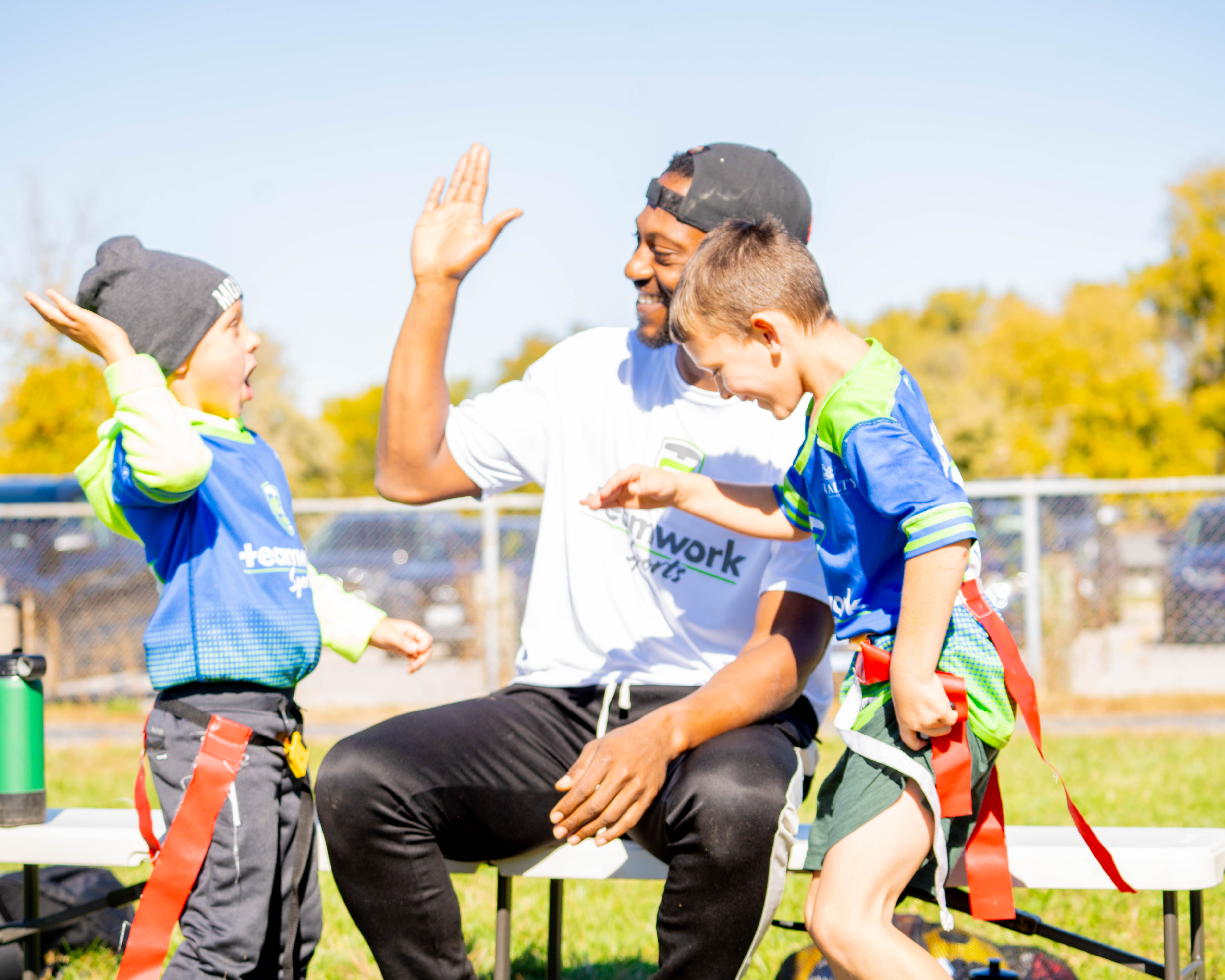 A Teamwork Sports coach high-fiving two young flag football players on the sideline